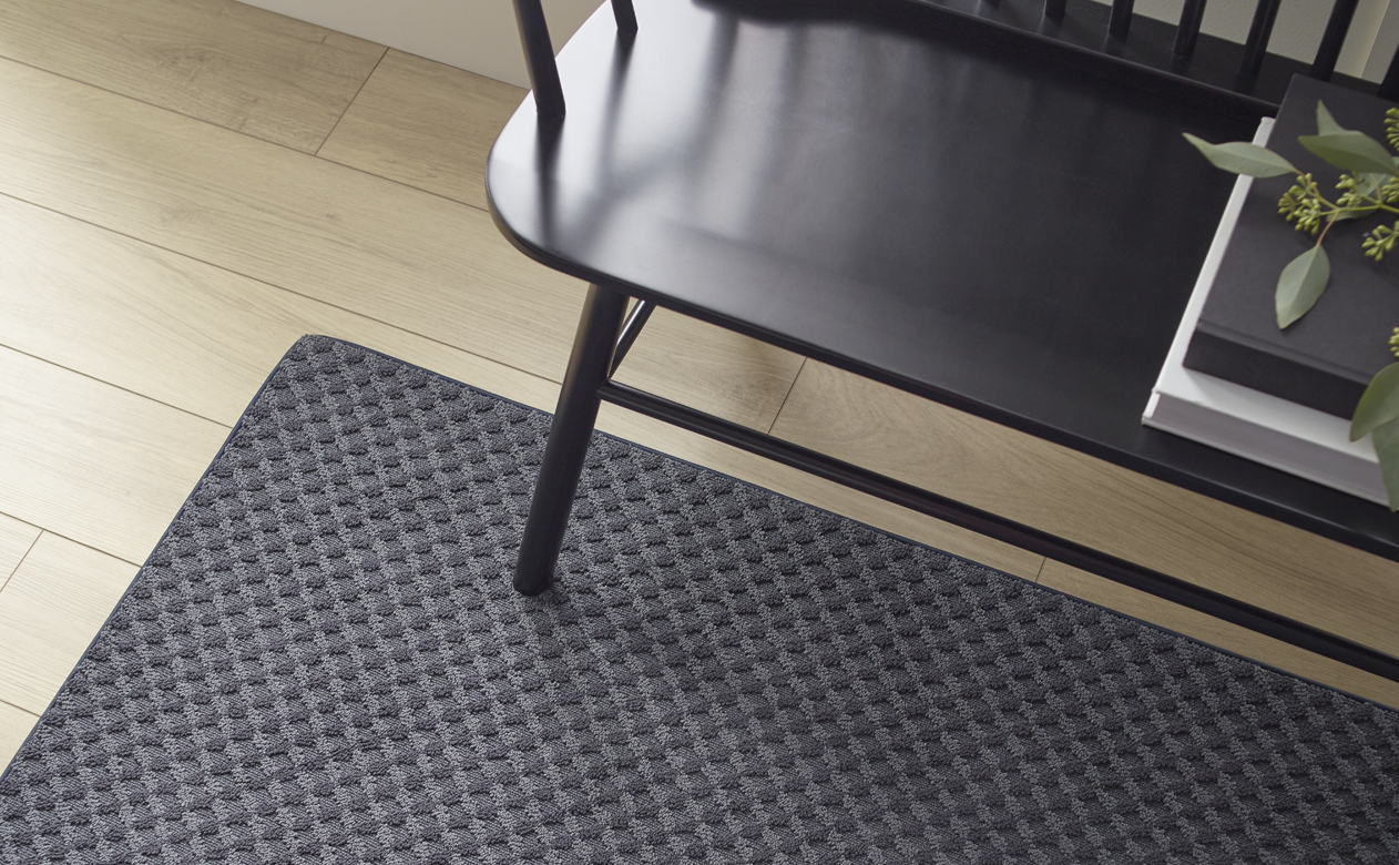 black textured area rug in entry way with black bench and light wood flooring